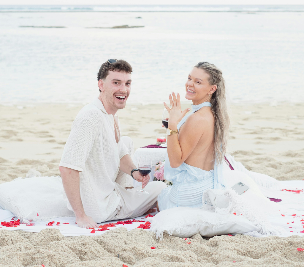 A couple sitting on the beach smiles and celebrates their love in a Tribute to Couples & Love – Meditation & Reiki Ceremony